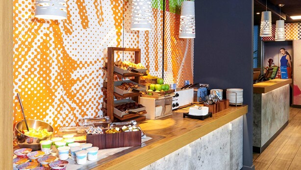 Zona de buffet con diversas opciones de comida, una barra con menú y una pared con un diseño colorido.