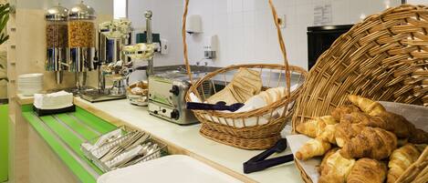 A buffet setup with various food items, including baskets of bread and pastries, and a coffee station.