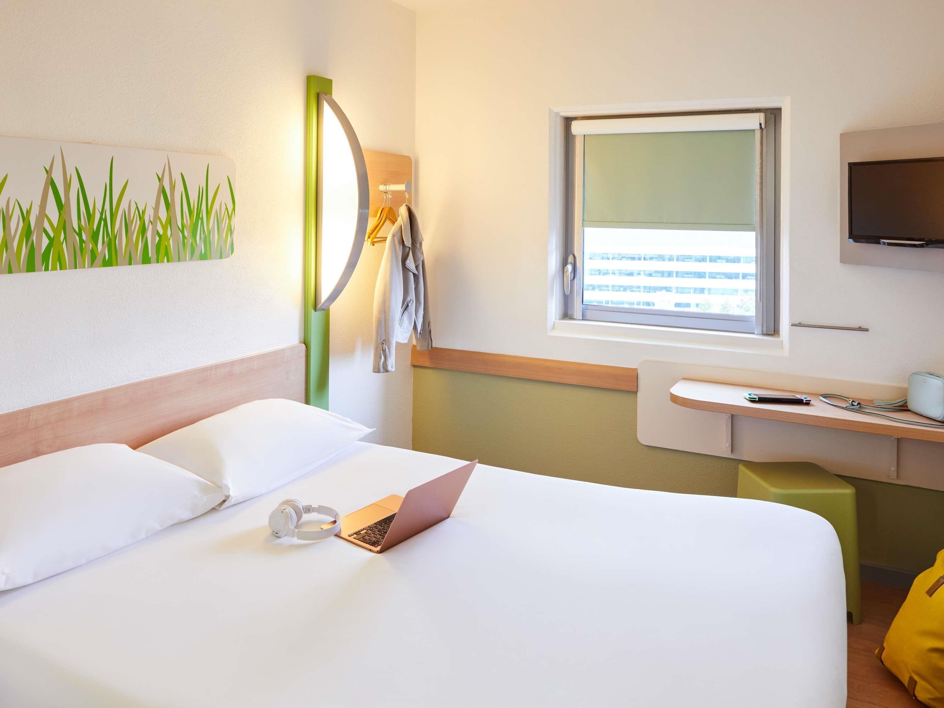 A hotel room with a bed, a desk with a laptop, headphones, and a TV.