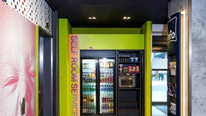 Una habitación luminosa y colorida con un refrigerador lleno de bebidas, un microondas y estantes con aperitivos.