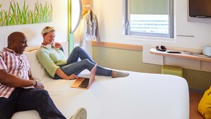 Una habitación con cama, un escritorio con computadora, televisión y ventana con persianas.