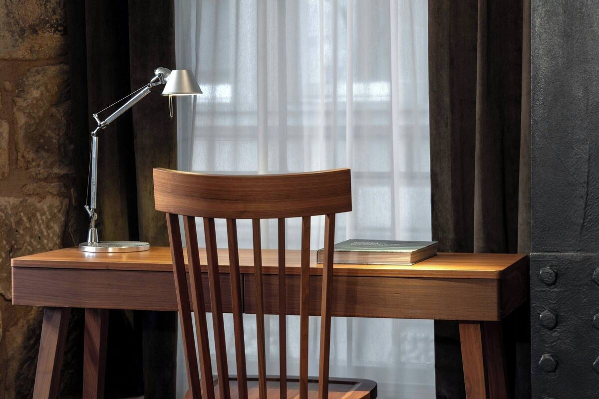 A wooden desk with a chair, a desk lamp, and a book.