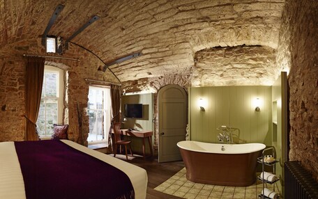 A bedroom with a large bed, a wooden desk, a bathtub, and a stone wall.