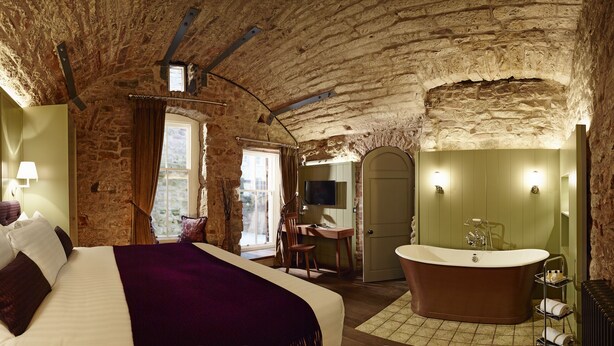 Ein Schlafzimmer mit einem großen Bett, einem Holztisch, einer Badewanne und einer Steinwand.