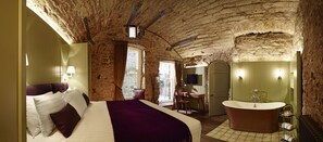 Ein Schlafzimmer mit einem großen Bett, einem Holztisch, einer Badewanne und einer Steinwand.