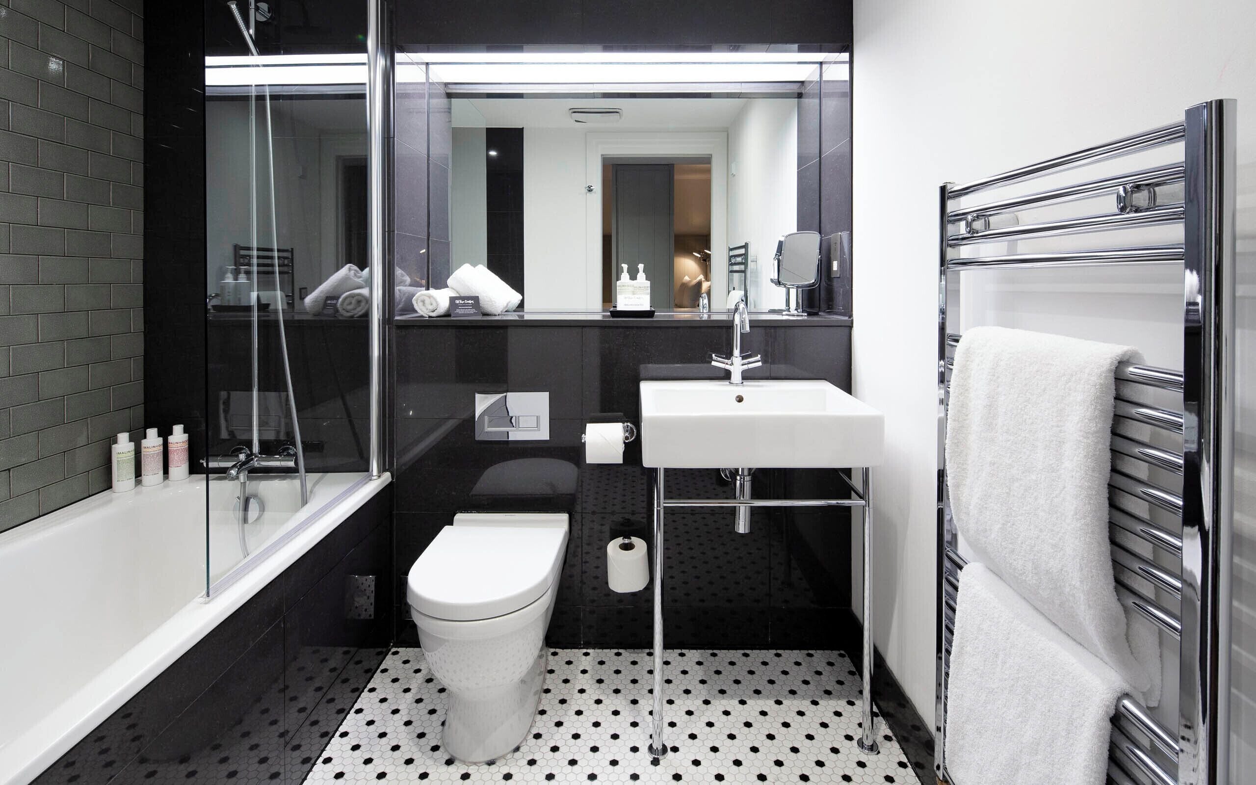 Un baño moderno con cabina de ducha de vidrio, inodoro blanco, lavamanos con grifo cromado y barra para toallas.