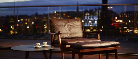 Un sillón de cuero y un reposapiés en un balcón con vistas a la ciudad de noche.