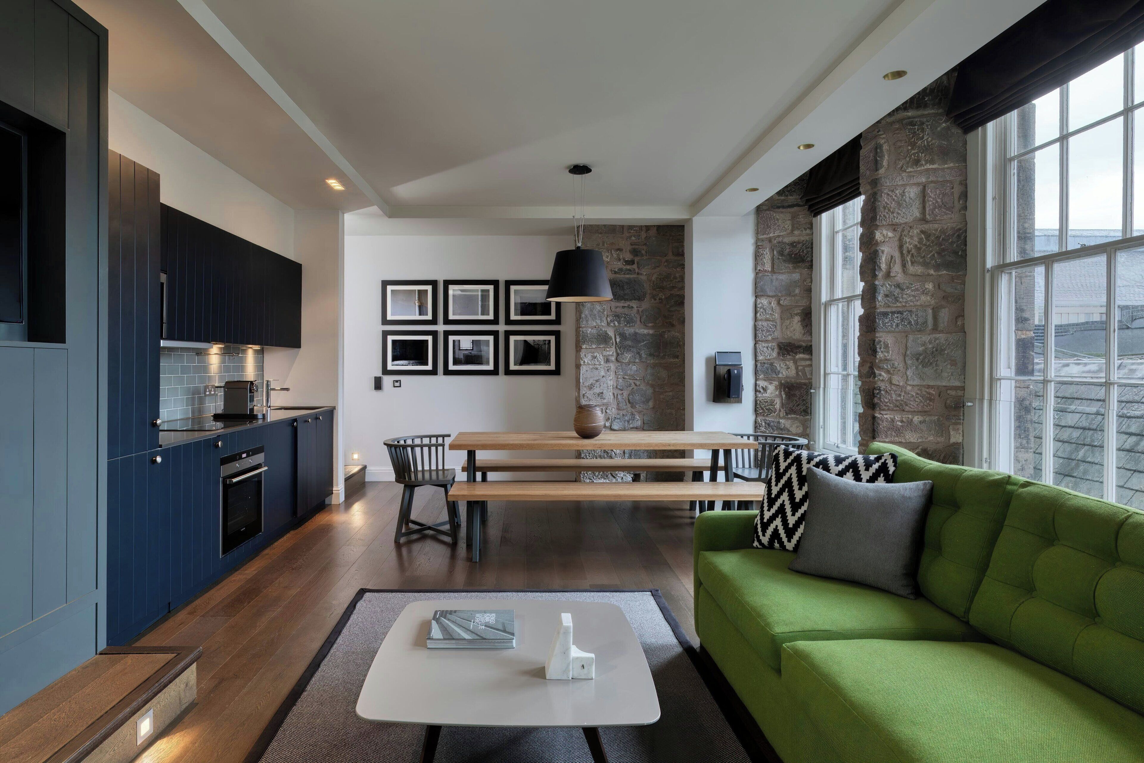 A modern kitchen with dark blue cabinets, a wooden dining table, and a green sofa.