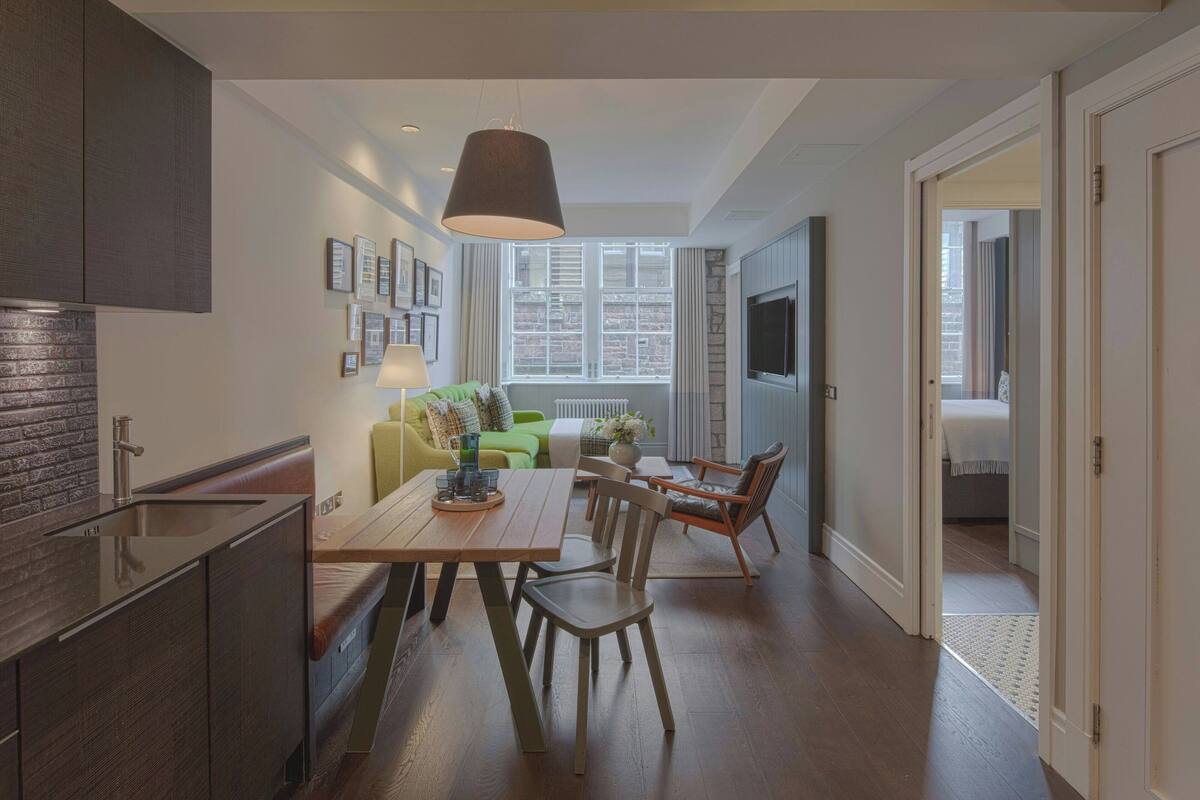 A modern kitchen with a built-in stove, a dining area with a wooden table and chairs, and a view of the city through large windows.