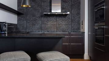 A modern kitchen with a dark brick backsplash, stainless steel appliances, and houndstooth-patterned stools.