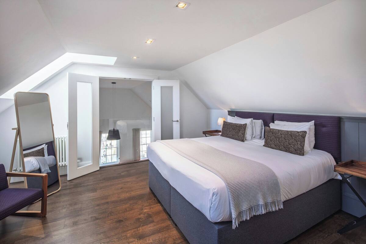 A modern bedroom with a large bed, a hanging chair, and a skylight.