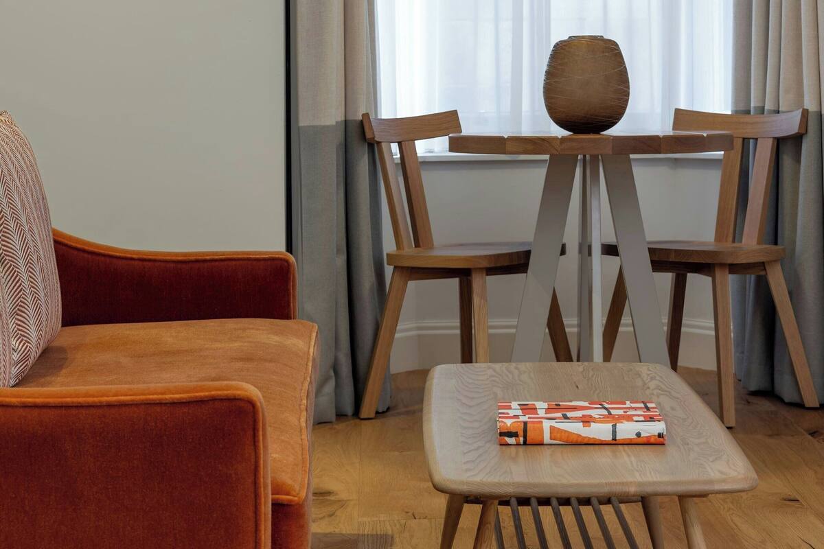 A modern living room with a wooden table, a cushioned chair, and a sofa.