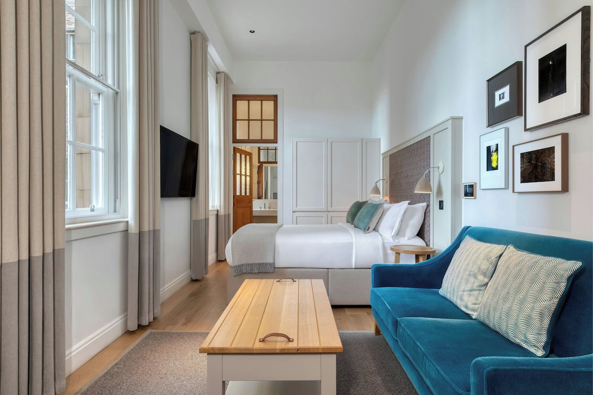 A modern hotel room with a bed, a blue sofa, a wooden coffee table, and a TV.