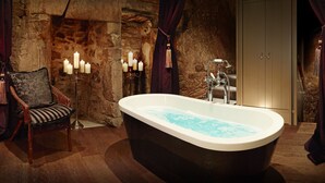Ein Badezimmer mit einer freistehenden Badewanne, einem Sessel und einer Wand aus Stein.
