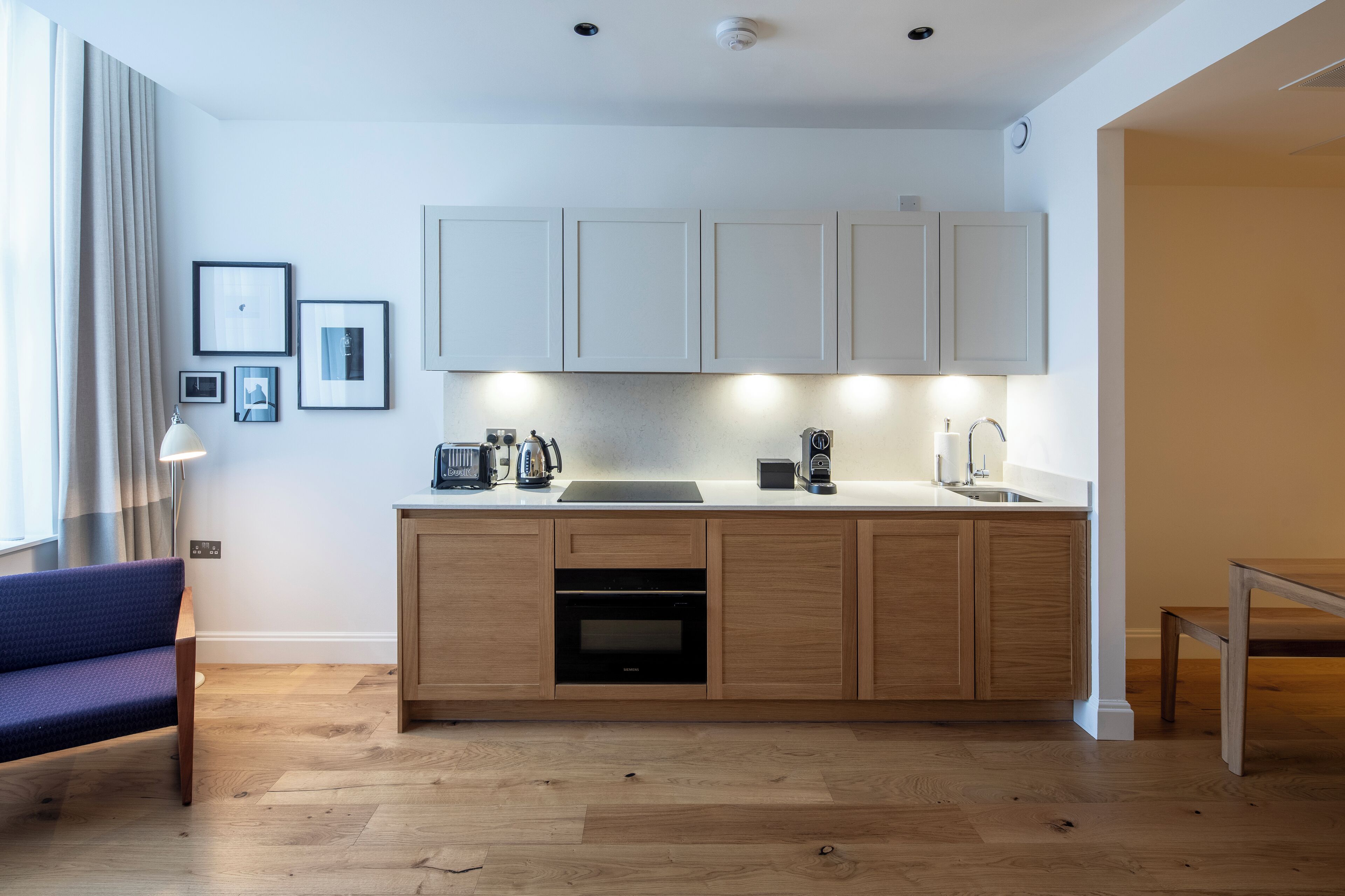 Una cocina moderna con armarios de madera, horno integrado y una encimera con una cafetera y otros electrodomésticos.