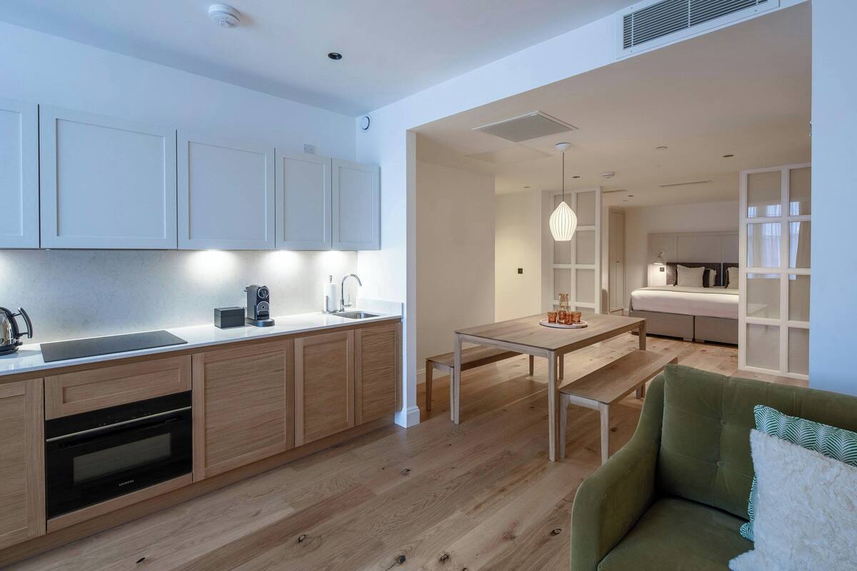 A modern kitchen with wooden cabinets, a built-in oven, and a dining area with a bench and table.