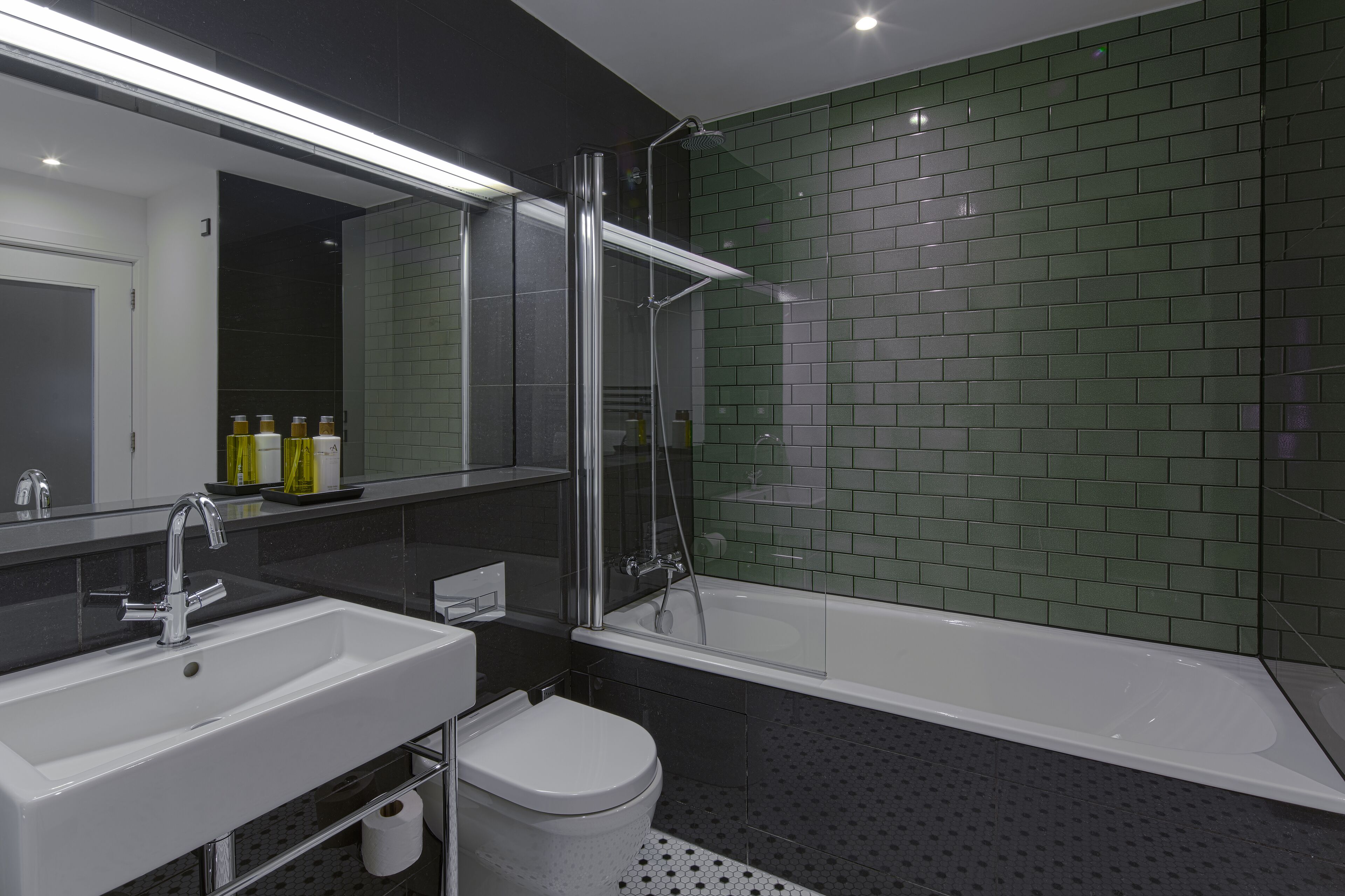 A modern bathroom with a white sink, a toilet, a glass-enclosed shower, and green-tiled walls.