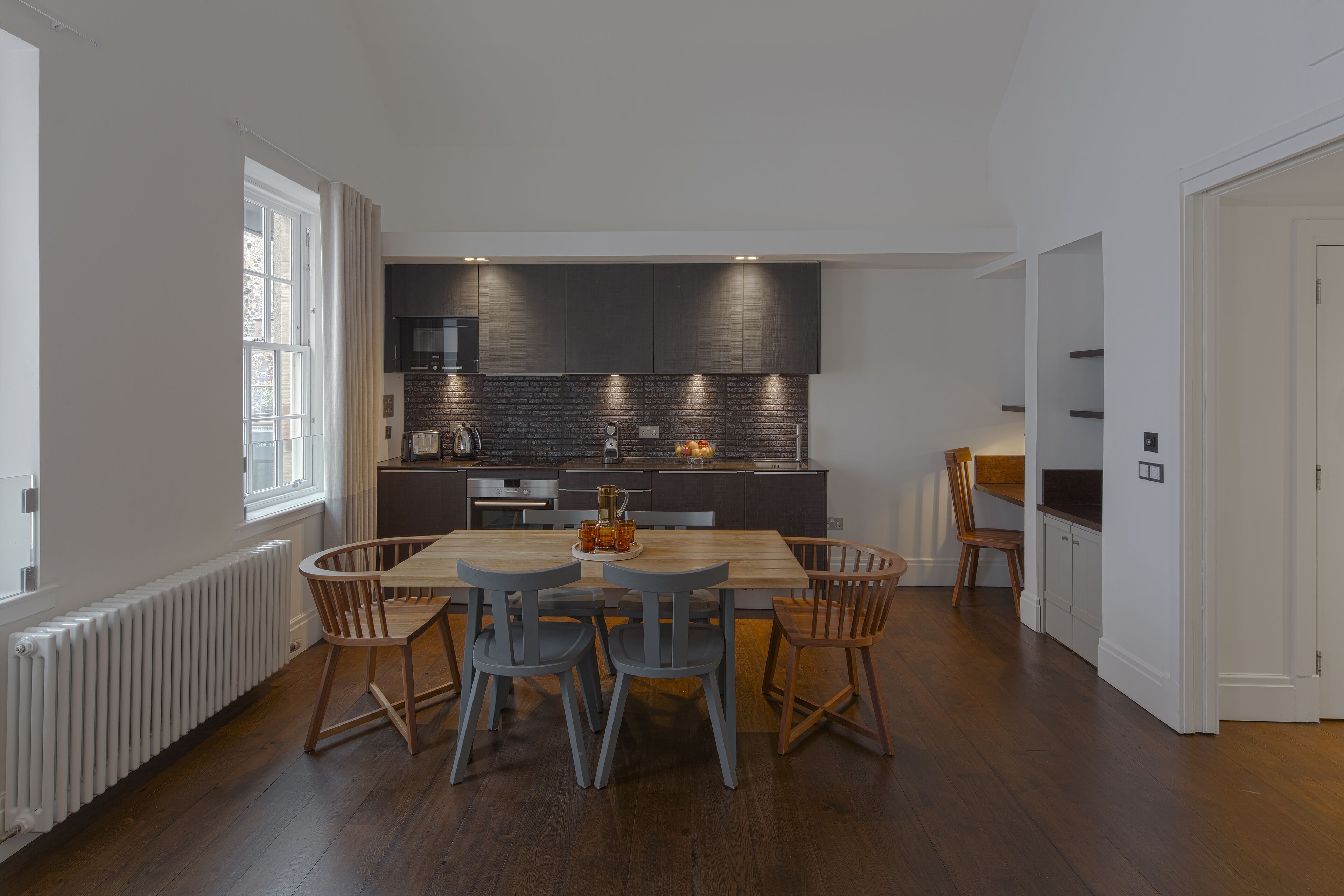 Una cocina moderna con armarios oscuros, una mesa de comedor de madera y dos sillas azules.