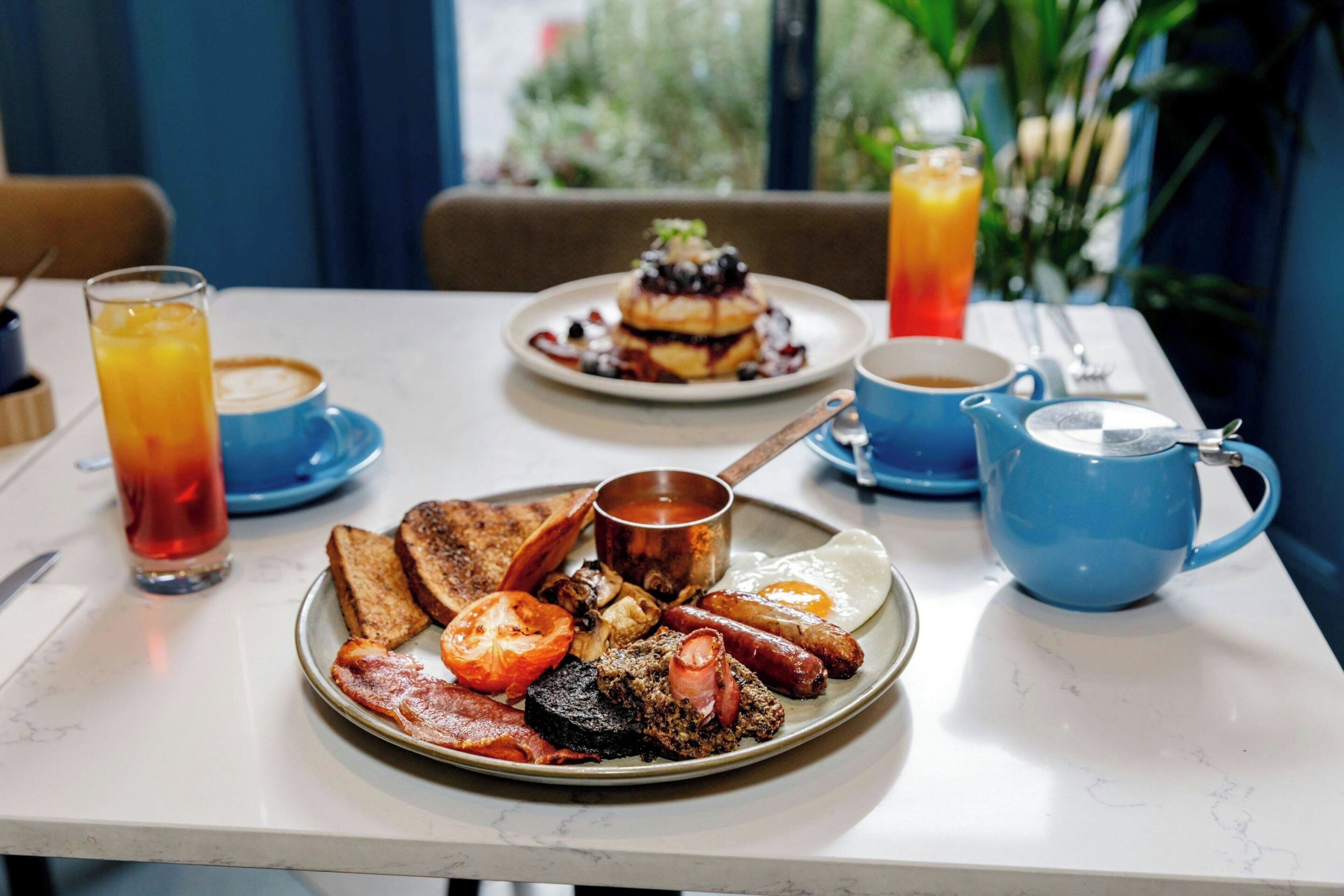 A breakfast plate with toast, bacon, eggs, sausages, and a small pot of jam.