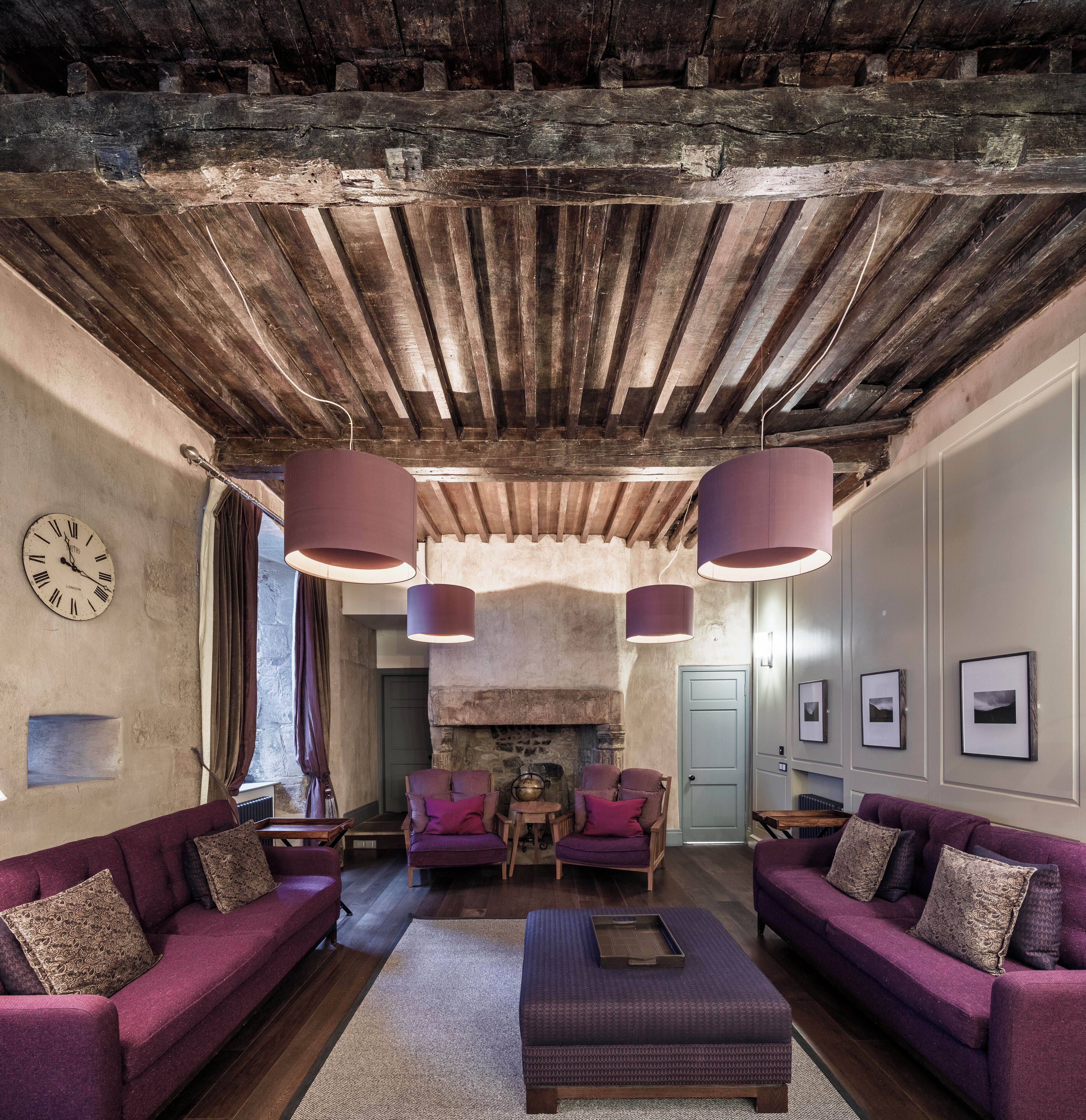 A rustic interior with exposed wooden beams, a fireplace, and purple upholstered furniture.