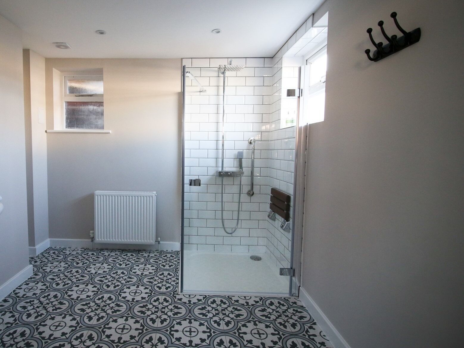 A modern bathroom with a shower, white tiled walls, a radiator, and patterned floor tiles.