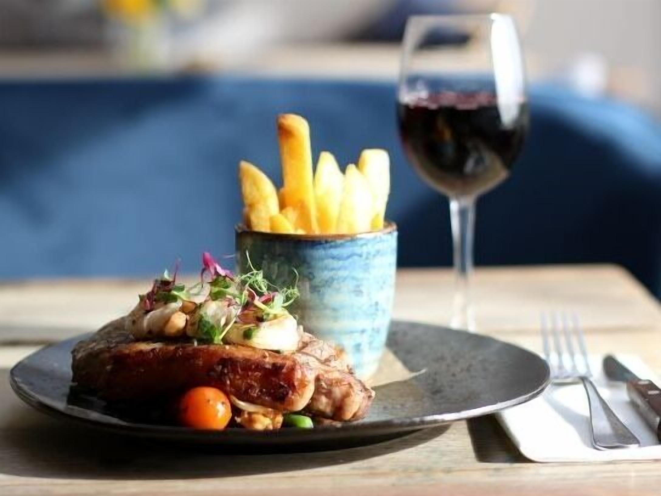 A plate with a steak, vegetables, and fries, accompanied by a glass of red wine.