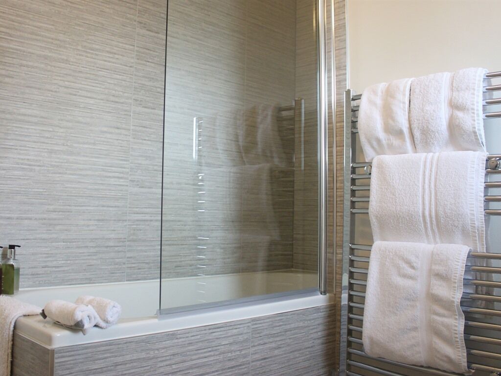 A modern bathroom with a glass shower enclosure, a white bathtub, and a towel rack with neatly folded towels.