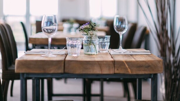 A dining table set with wine glasses, water glasses, and a small vase with flowers. - The Cliff House Hotel (New Milton)