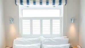 A bedroom with a bed, a window with shutters, a hanging light fixture, and bedside tables with a phone and a lamp. - The Cliff House Hotel (New Milton)