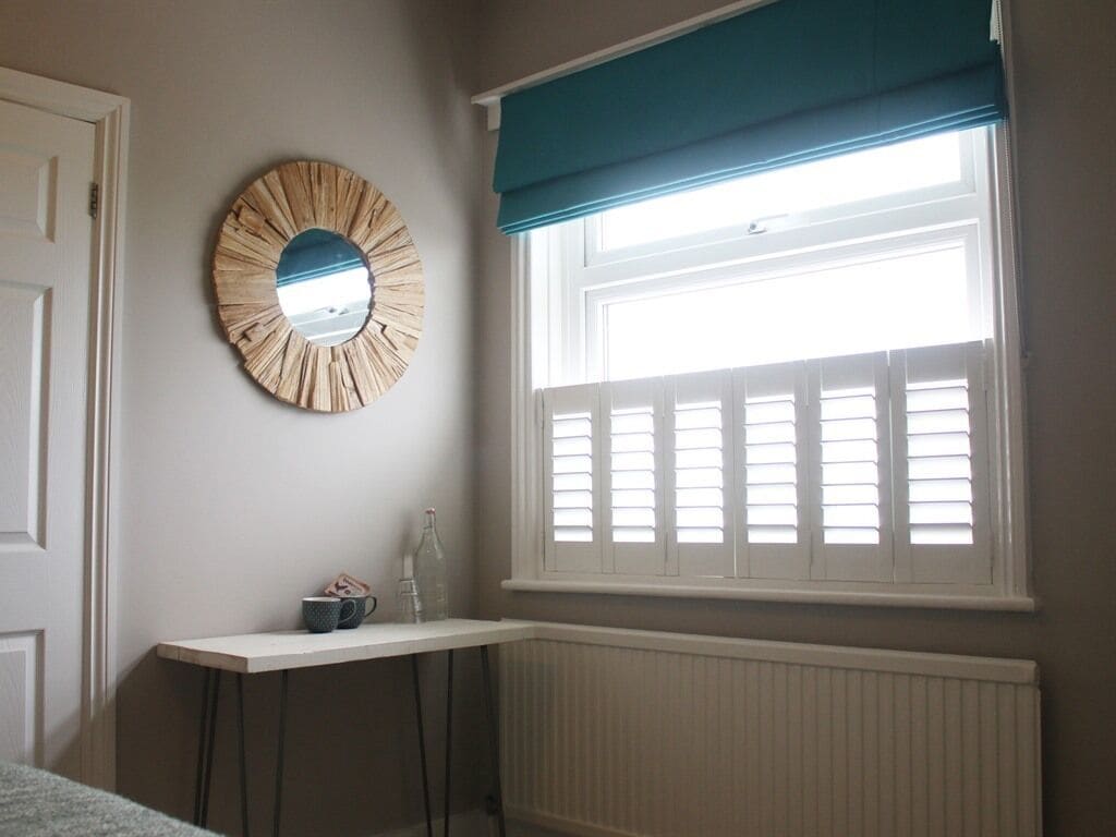 Ein Zimmer mit Fenster, Spiegel, Heizkörper und einem kleinen Tisch mit Flasche und Tasse.