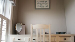 A bedroom with a wooden chair, a dresser with drawers, a mirror, and a framed picture on the wall. - The Cliff House Hotel (New Milton)