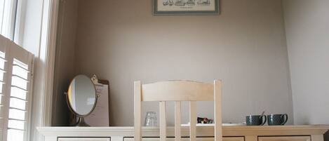 A bedroom with a wooden chair, a dresser with drawers, a mirror, and a framed picture on the wall.