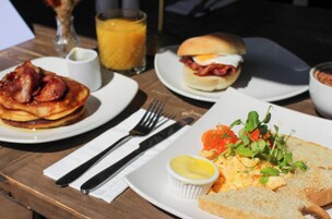 A breakfast setting with pancakes, a sandwich, and a plate with scrambled eggs and greens.