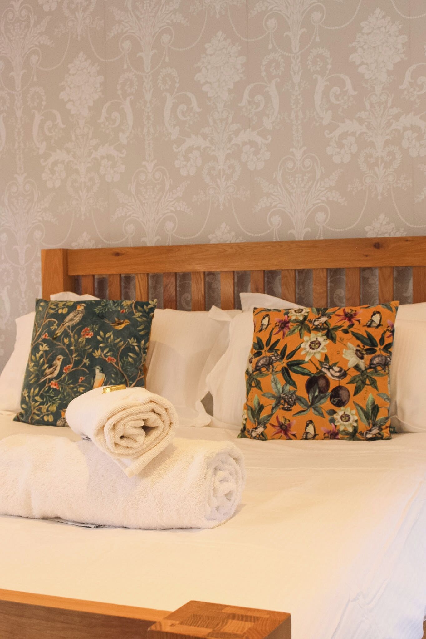 A bed with a wooden headboard, two pillows with floral patterns, and a rolled white towel.