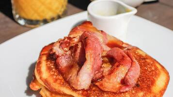 Un plato de panqueques con tocino y jarabe, un vaso de jugo de naranja y una taza de café con azúcar.