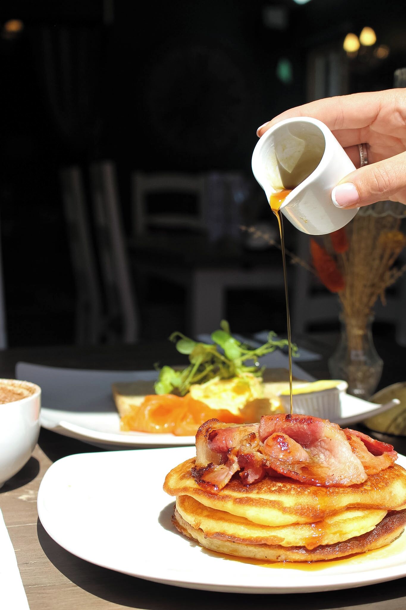 Un plato de desayuno con panqueques y tocino, con jarabe siendo servido.