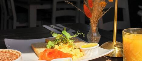 A breakfast setting with a plate of pancakes, a glass of orange juice, and a small vase with dried flowers.