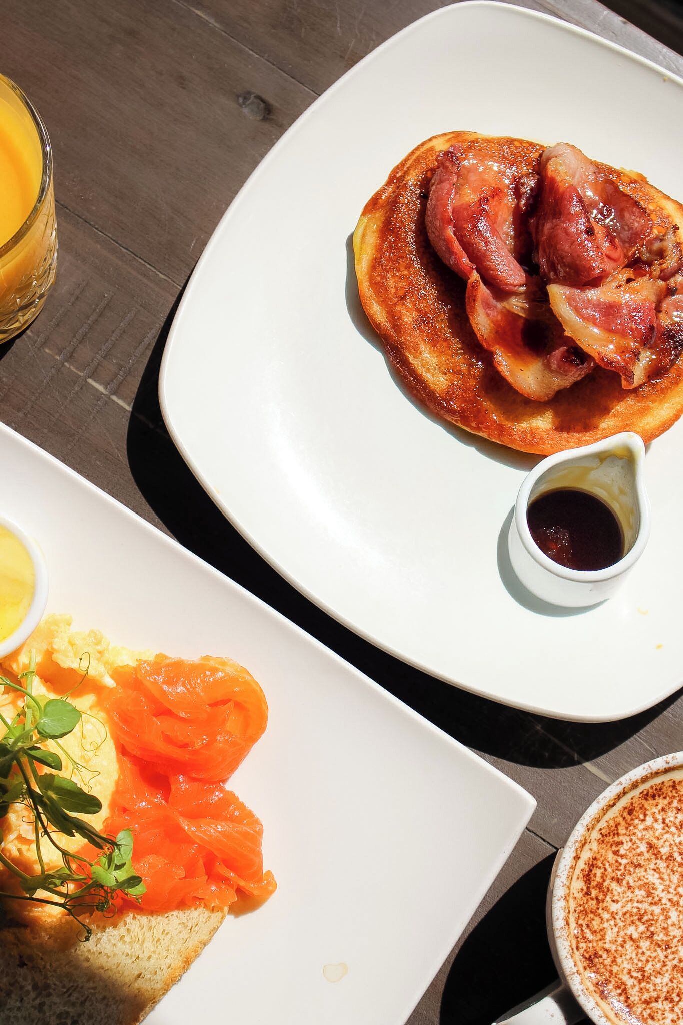 Un desayuno con tocino, un recipiente pequeño de salsa y salmón ahumado sobre tostada.