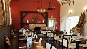 A restaurant with a brick fireplace, wooden tables and chairs, and a red accent wall. - The Selsey Arms (Chichester)