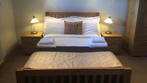 A neatly made bed with white linens, two bedside lamps, and a wooden headboard. - The Selsey Arms (Chichester)