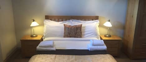 A neatly made bed with white linens, two bedside lamps, and a wooden headboard.