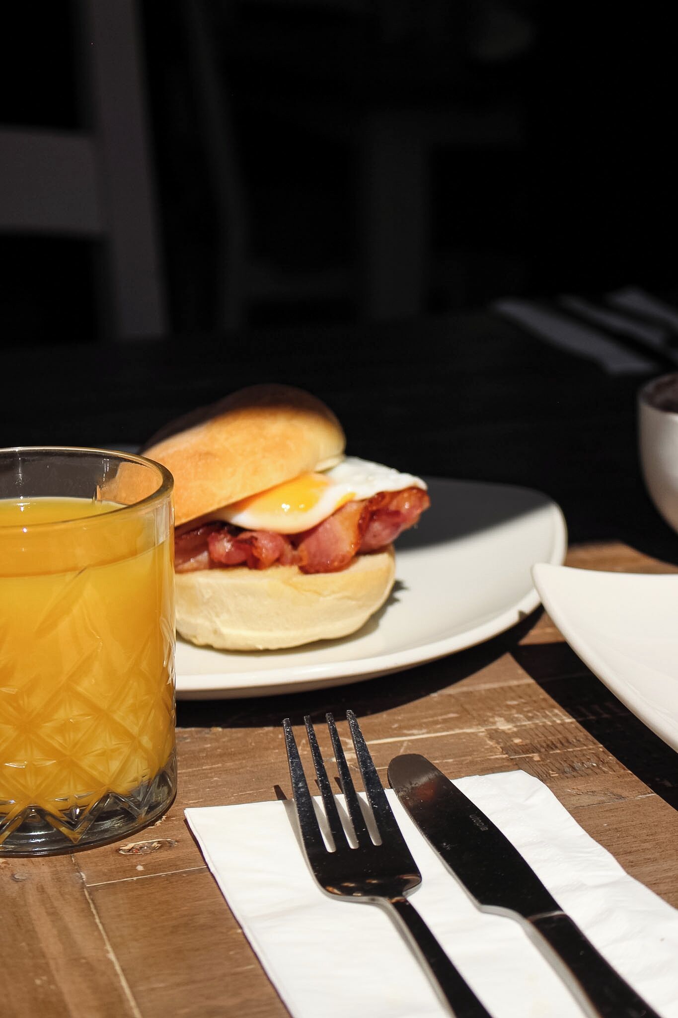 A breakfast setting with a sandwich, a glass of orange juice, and cutlery on a wooden table.