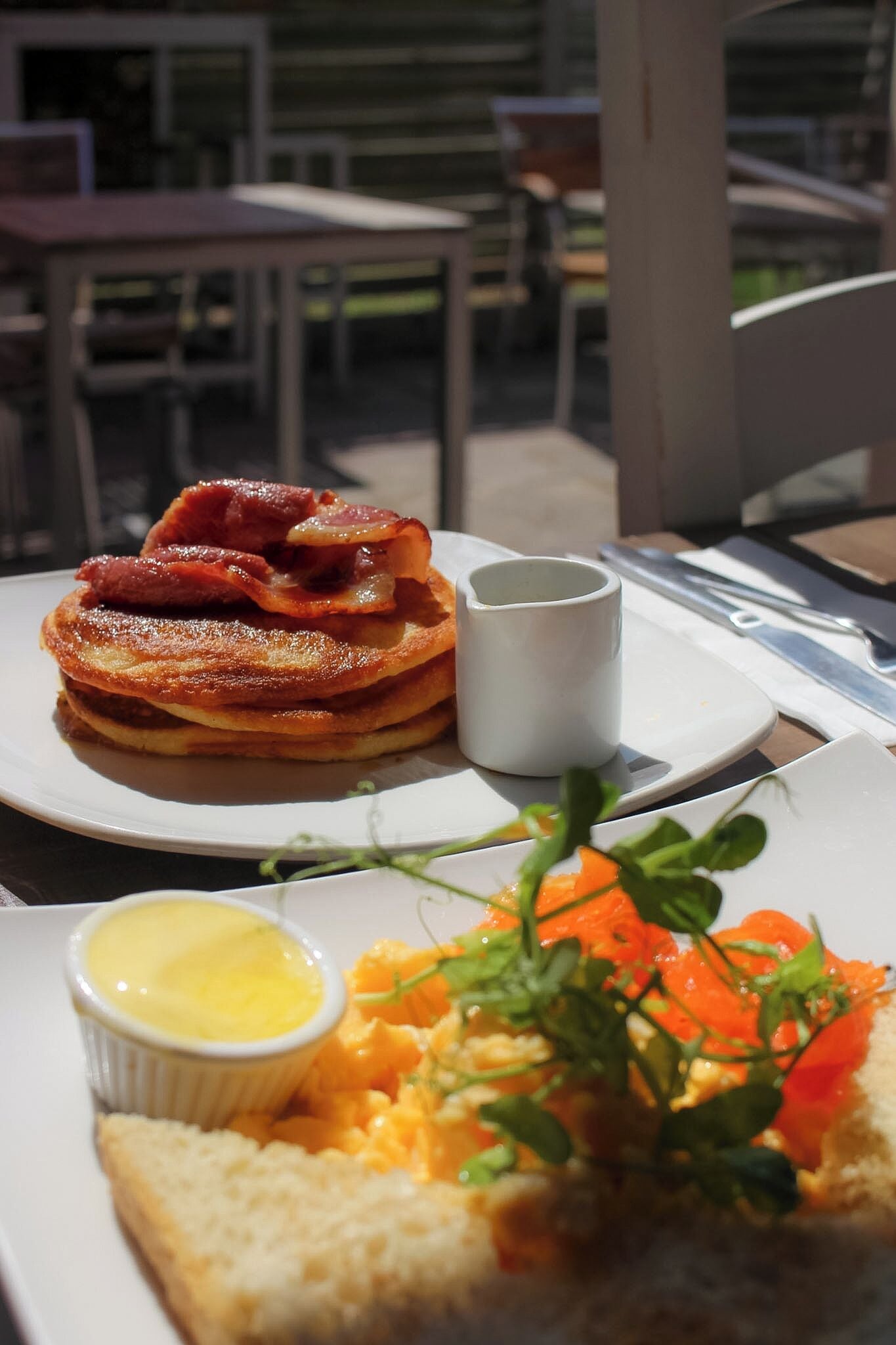 A breakfast setting with pancakes, bacon, and a side of scrambled eggs and smoked salmon.