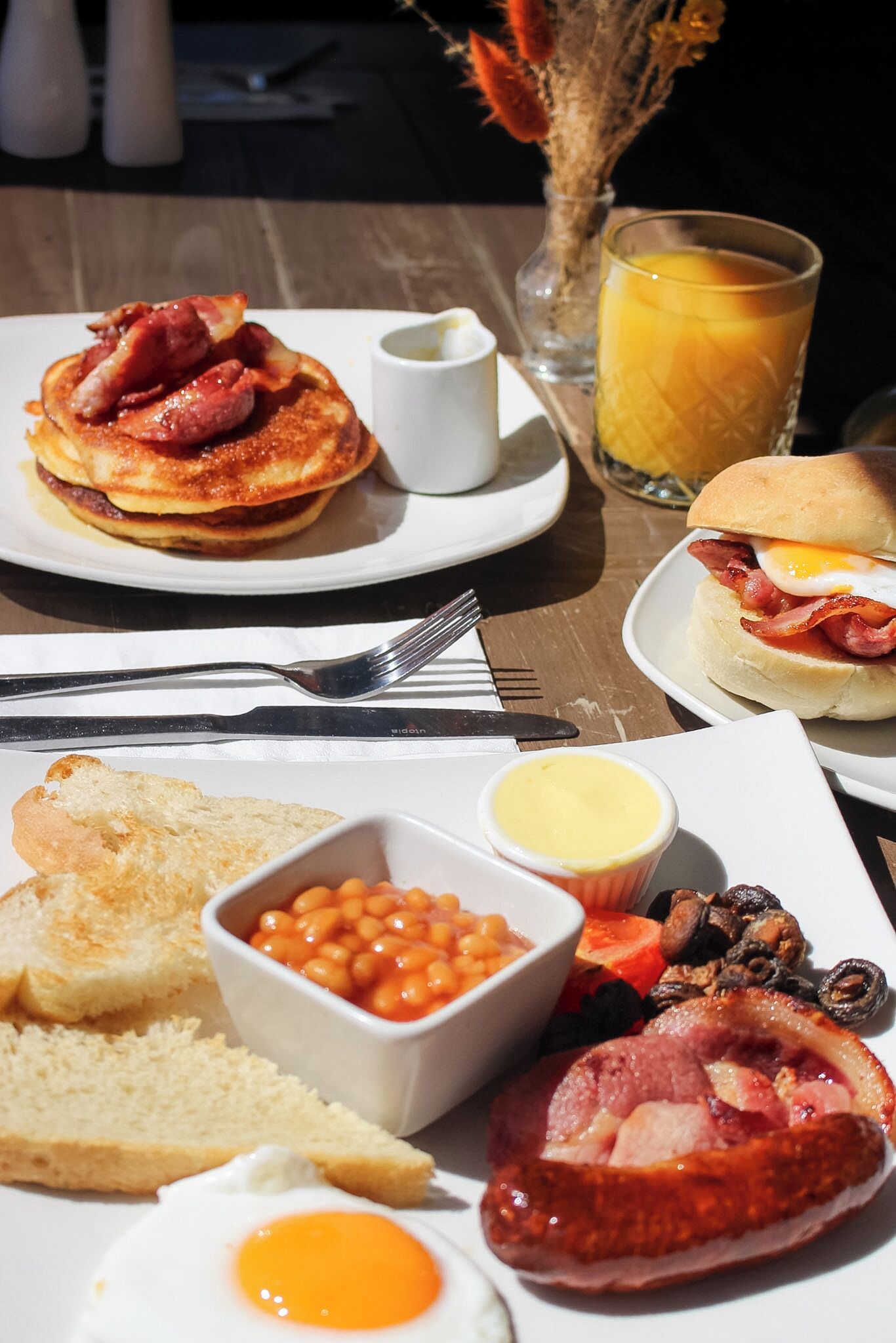 A breakfast setting with pancakes, eggs, toast, beans, and a glass of orange juice.