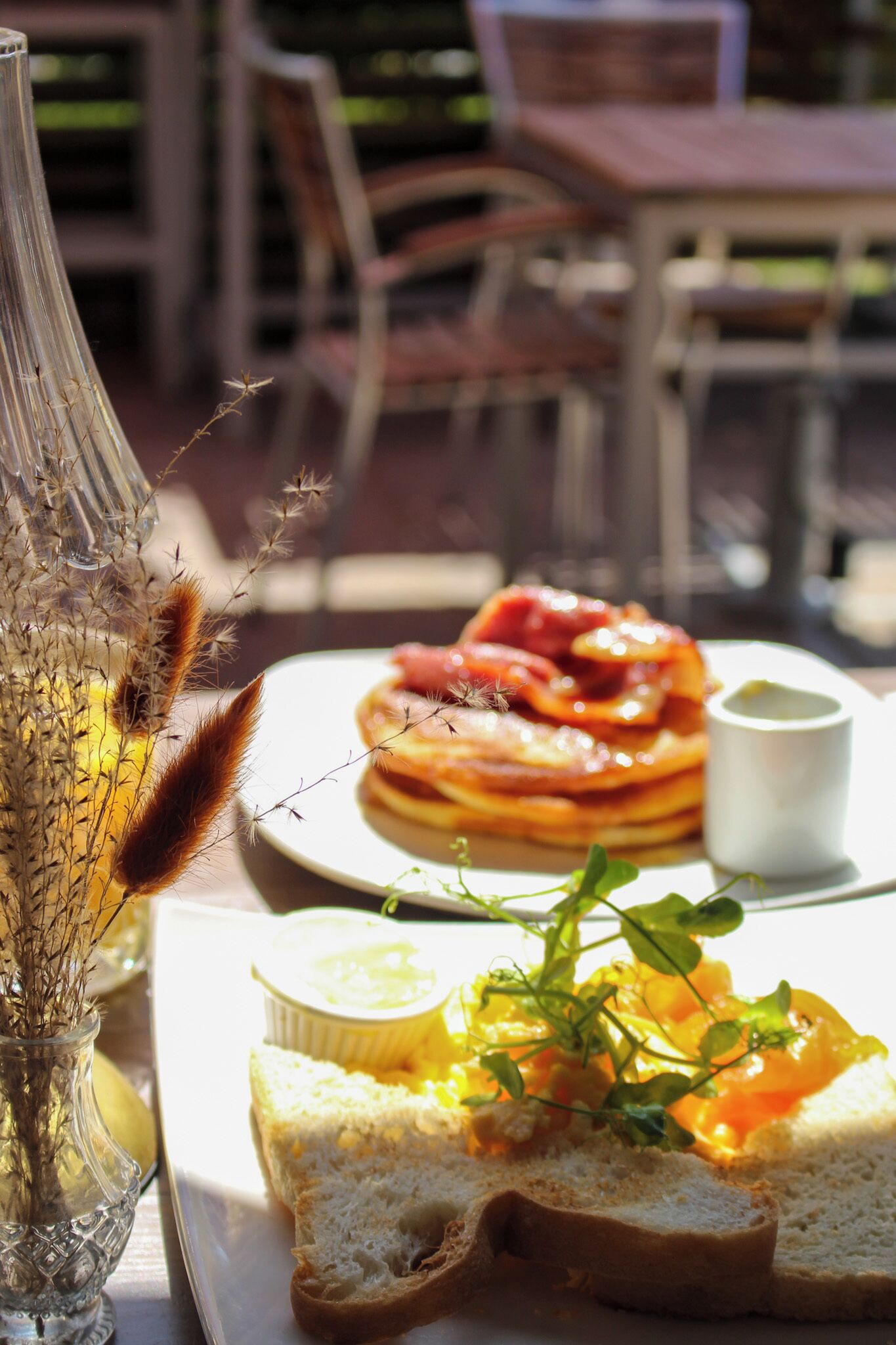 Une table avec une assiette de nourriture, un vase en verre contenant des plantes séchées et une tasse blanche.
