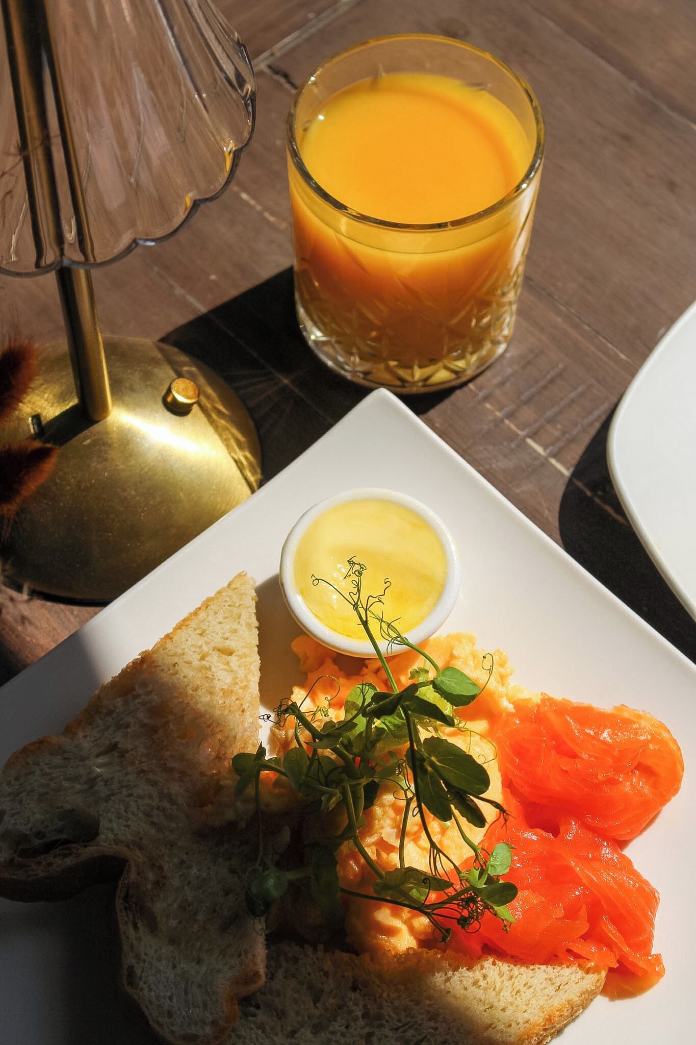 A table setting with a plate of food, a glass of orange juice, and a small bowl of butter.