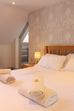 A hotel room with a neatly made bed, a nightstand with a lamp, and a bathroom visible through an open door. - The Selsey Arms (Chichester)