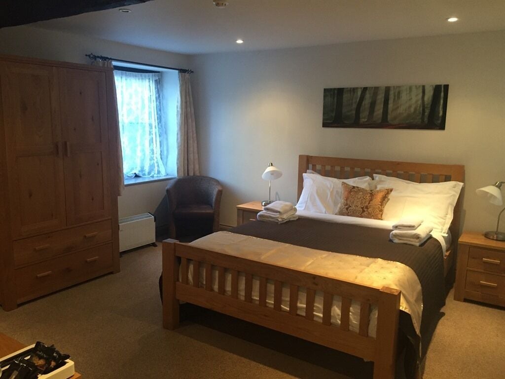 Une chambre à coucher avec un lit en bois, une table de chevet, une chaise, une armoire et une fenêtre avec des rideaux.