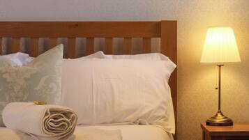A neatly made bed with a rolled towel, a bedside lamp, and a wooden nightstand.