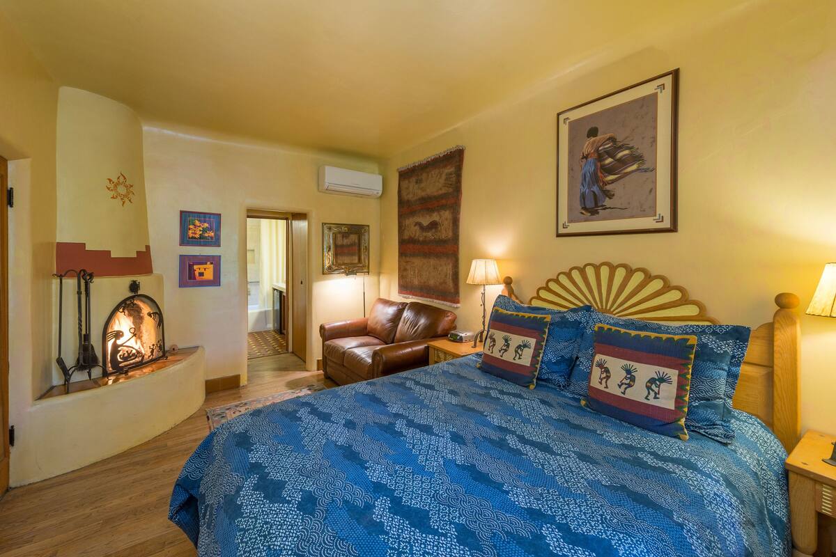A bedroom with a large bed, a leather armchair, a nightstand, and a wall-mounted lamp.
